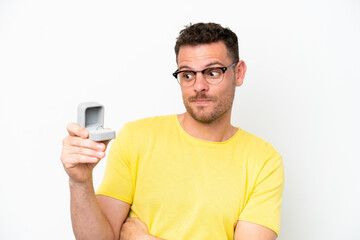 Young caucasian man holding a engagement ring isolated on white background with sad expression