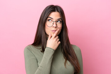 Young Brazilian woman isolated on pink background With glasses and having doubts