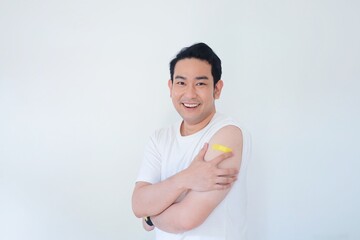 Smiling Asian man showing Vaccinated Shoulder, Asian man with medical plaster on his arm.