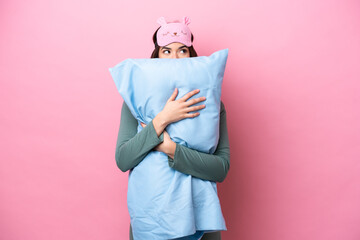 Young Brazilian woman isolated on pink background in pajamas and holding a pillow