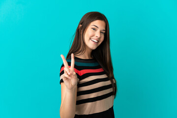 Teenager Brazilian girl over isolated blue background smiling and showing victory sign
