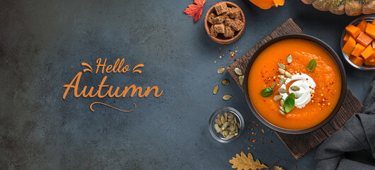 Pumpkin soup with cream and basil on a dark background. Top view, copy space