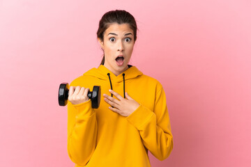 Young sport girl making weightlifting over isolated pink background surprised and shocked while looking right