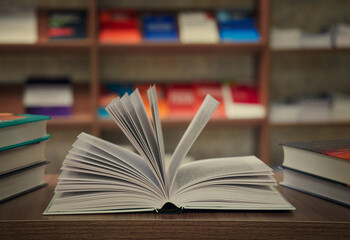 The concept of teaching education with the opening of a book or textbook in an old library, a stack of piles of literary text, an academic archive on the reading table and the passage of bookshelves i