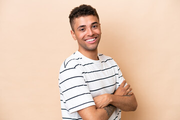 Young Brazilian man isolated on beige background with arms crossed and looking forward