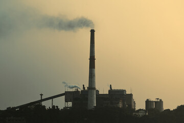 Fototapeta na wymiar Factory chimney emitting smoke at a thermal power station beside Ganges river. Photo taken during dusk.