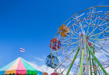 The old colorful Ferris wheel with fluorescent lamp decoration and carousel tent against blue sky...