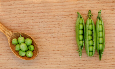 Fresh three green peas on wood texture background. Pea pods are opened. Wood spoon is on other side full of peas