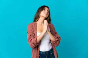 Young caucasian woman isolated on blue background keeps palm together. Person asks for something