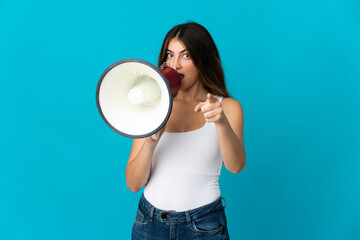 Young caucasian woman isolated on blue background shouting through a megaphone to announce something while pointing to the front