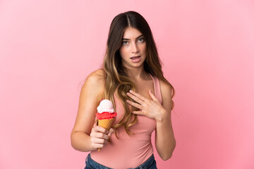 Young caucasian woman with a cornet ice cream isolated on pink background surprised and shocked while looking right