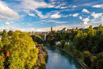Fototapeta na wymiar Stunning panoramic view of riversides of Aare river in Bern city, Switzerland. Arch bridge, rooftops and tower of Munster cathedral. Snowcaped alpine peaks on background. Picturesque sky