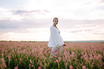Fototapeta na wymiar Young woman in stylish summer dress feeling free in the field with flowers. Nature, fashion, vacation and lifestyle