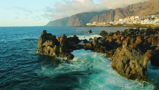 Touristic spot. Aerial sunset light on ocean waves and rocks. Tenerife, Canary Island, town Puerto de Santiago, Charco el Diablo or natural pool of Devil. Lava flows, volcanic bizzare stone beach