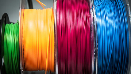 Colorful spools of filament for 3D printing – green, orange, red and blue plastic wires on reels, close-up view of materials used in FDM/FFF 3D printers for prototyping and manufacturing