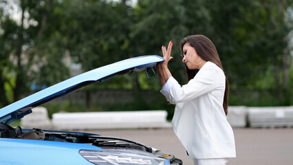 Businesswoman driver carefully examines condition of car engine under hood. Modern vehicle needs...