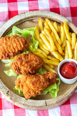 Spicy chicken wings, with fries lettuce and ketchup, on a rustic wooden platter plate.  On a gingham tablecloth
