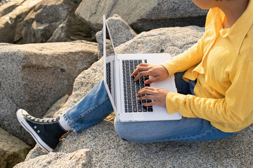 Anonymous young man using laptop on rocky coast