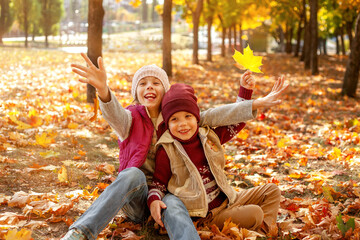 happy boy and girl laughing on the background of autumn leaves in the park. Family Having Fun Outdoors. Yellow Trees and Leaves.