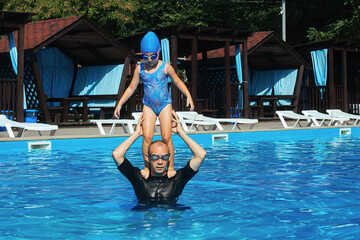 Individual swimming lessons with children in the outdoor pool during the warm season. The coach teaches a sports girl to keep balance and dive into the water of the pool from his shoulders correctly