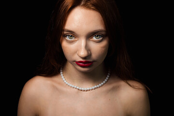 Portrait of a girl on a black background. Beautiful red-haired girl with red lipstick on her lips.