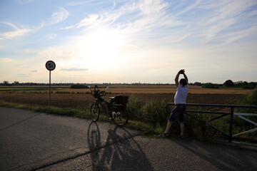 Mężczyzna z podniesionymi rękoma i rowerem turystycznym na tle zachodzącego słońca.