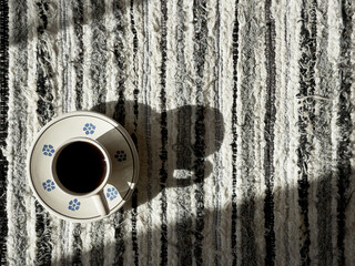 Morning coffee cup on the strapped woven tablecloth still life with window light. Cozy home and beverages concept image.