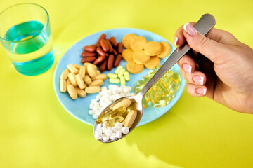 A handful of pills, capsules and multi-colored tablets on a plate next to cutlery. Taking medication. Pills instead of food. The concept of vitamins instead of food