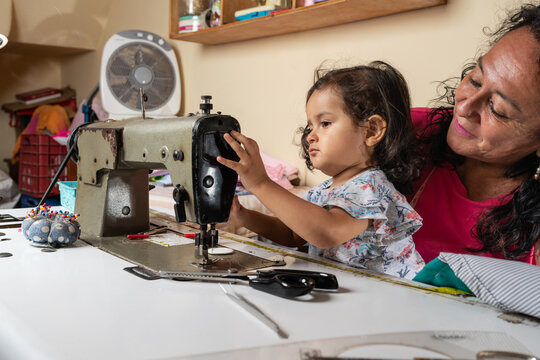 Hispanic woman with granddaughter working on sewing machine