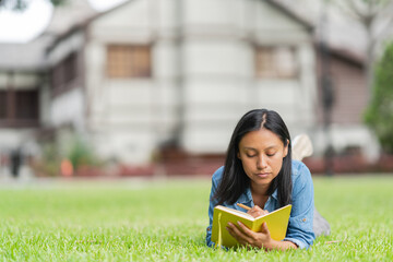 Ethnic woman lying on the grass and taking notes in notepad