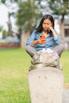 Bored ethnic woman scrolling smartphone in park