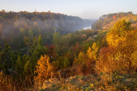 Autumn scenery with colorful trees on the rocky hillsides of Teteriv river banks. Yellow and red foliage illuminated with rising sun. Zhytomyr, Ukraine.