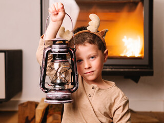 Cute boy in reindeer antlers near kerosene lamp