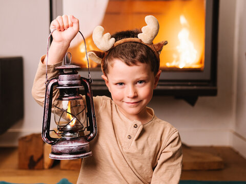 Cute boy in reindeer antlers near kerosene lamp