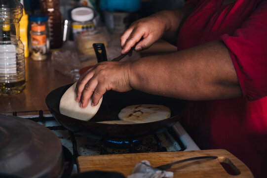 Crop ethnic woman frying arepas in pan at home