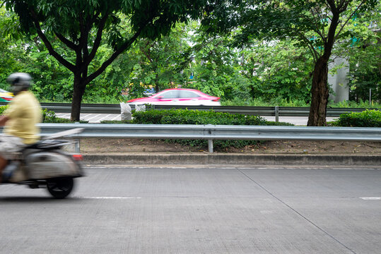 A Man On Motorbike Moving Fast, Blurred Motion. Biker Ride Along The Road In Green Urban Area.