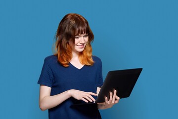 Red-haired teenage girl with laptop on blue background.