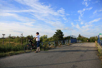 Mężczyzna z rowerem turystycznym na tle wiaduktu kolejowego.