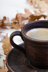 a clay cup with freshly brewed coffee and beautiful autumn oak leaves and acorns in a chaotic order on a white slate or stone background lie in a chaotic order. view from above.