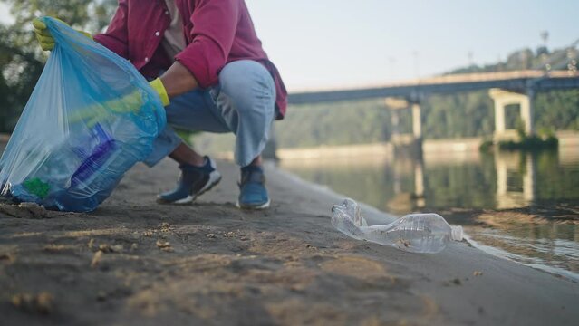 African American man gathers trash in bag squatting by water