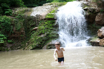 Fototapeta na wymiar Happy child bathing in Rufabgo stream next to waterfall Shum