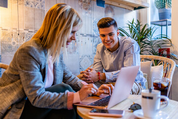 Happy coach with laptop talking to male employee in cafe