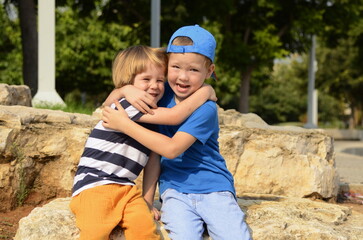 Two little boys, two friends, brothers are sitting on the street embracing. Concept: friendship, family, adventure, childhood, preschool education, kindergarten, amusement park, traveling with childre