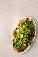 Salad of fresh farm vegetables in an oval dish on a pink background, sitya lettuce and chard, tomatoes and colorful bell peppers, arugula and sesame seeds