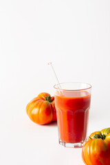 Homemade freshly squeezed tomato juice in a glass with a glass straw and tomatoes on a white background