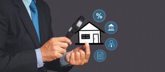 A businessman's holding a magnifying glass and looking at a home property while standing over gray...
