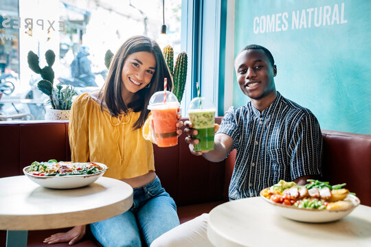 Multiethnic Friends With Smoothies Speaking On Sofa In Restaurant