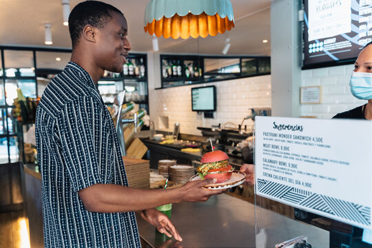 Smiling man with delicious hamburger at counter in restaurant