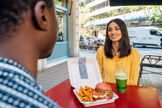 Content woman talking to crop ethnic friend at restaurant table
