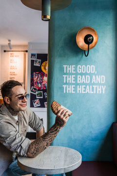 Crop tattooed person with delicious sandwich in restaurant